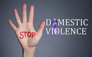Female hand with text STOP DOMESTIC VIOLENCE on grey background