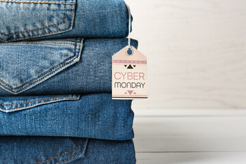 Stack of jeans clothes and tag with text CYBER MONDAY on table, closeup