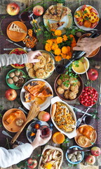 Country style. Thanksgiving table. Lots of food. Guests pour red wine into a glass. Guests are holding food with their hands over the set table. View from above.