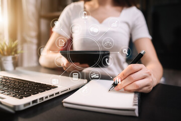 Female businessman hand working at a tablet and writing on a notepad with a pen in the office. on the wooden desk there a graph business diagram.