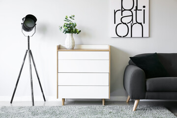 Modern chest of drawers with sofa and lamp near light wall in room - obrazy, fototapety, plakaty