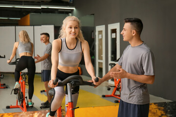 Young woman with coach training on exercising bike in gym