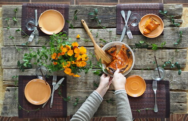 Thanksgiving wooden ancient table setting process. Hostess hands lay pumpkin on plates. Rustic style.