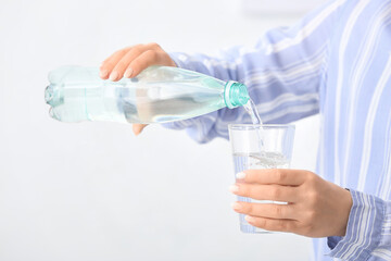 Woman pouring water from bottle into glass on light background