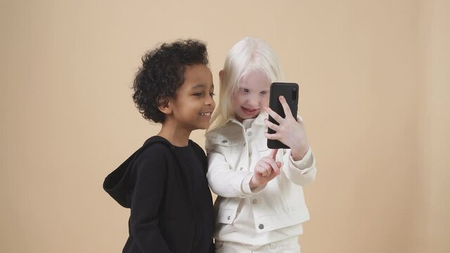 Happy little children pose in studio and take selfi on smartphone, modern generation and gadgets.