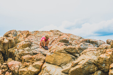 Solve humanity problem for new generation. Sad Child boy sit squatting on beautiful natural composition brown stone rock shabby cliff cracks high mountain, copy space cloud. Nature after pandemic