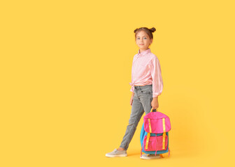 Little schoolgirl with backpack on color background