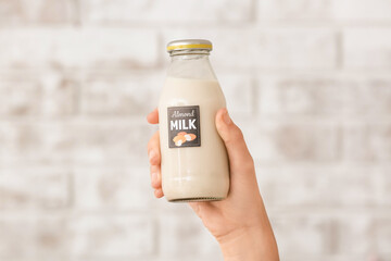 Female hand with bottle of almond milk on brick background