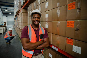 Mixed race male worker smiling with crossed arms leaning against parcels in factory shop