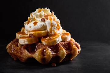 Waffles with bananas topped with caramel syrup on a dark stone background
