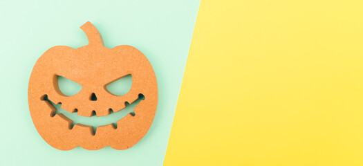 Halloween background idea.Flat lay wooden Jack o lantern spooky pumpkin on green yellow paper color background.Halloween design with copy space for text advertising.Background idea in Autumn October.
