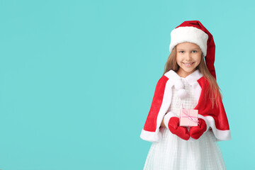 Cute little girl in Santa Claus costume and with Christmas gift on color background