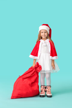 Cute little girl in Santa Claus costume and with Christmas bag on color background