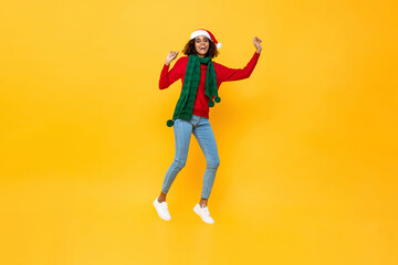 Fototapeta na wymiar Excited pretty woman in Christmas attire jumping on isolated yellow studio background