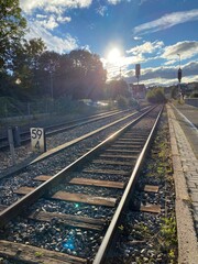 Fototapeta premium Bahngleise führen in den Horiznt die Sonne scheint entgegen bei blauem Himmel mit weißen Wökchen