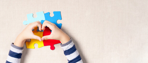 Top view & banner, a beautiful hands of little autistic child making heart shape over symbol colored puzzle pieces. Supportive, World autism awareness day, Caring & Understanding love concept. - obrazy, fototapety, plakaty