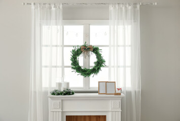 Beautiful Christmas wreath hanging on window near fireplace in room