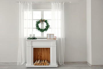 Beautiful Christmas wreath hanging on window near fireplace in room