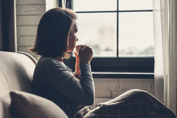 Back view of lonely сaucasian young woman enjoying having breakfast with cup of hot coffee and...