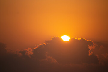 Golden sun rising behind the clouds in an orange sky