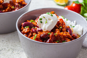 Chili con carne with rice in gray bowl. Beef stew with beans in tomato sauce with sour cream and rice. Traditional Mexican food concept.