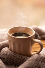 Steaming coffee cup and knitted sweater on a blurred background. Beige colors, autumn mug, autumn coffee. Banner space mock up for adding text.