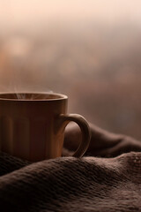 Steaming coffee cup and knitted sweater on a blurred background. Beige colors, autumn mug, autumn...