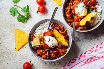 Chili con carne with rice, sour cream and nachos in gray bowl. Beef stew with beans, tomato sauce,  sour cream and rice. Traditional Mexican food concept.
