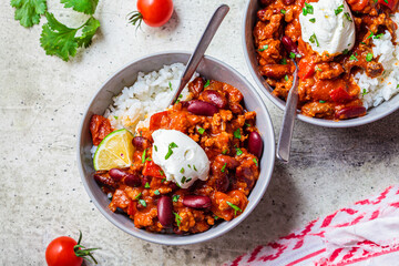 Chili con carne with rice in gray bowl, top view. Beef stew with beans in tomato sauce with sour cream and rice. Traditional Mexican food concept. - obrazy, fototapety, plakaty