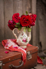 Still-life. A bouquet of red roses in a vase on a suitcase.