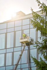 A worker in overalls on an elevator washes the glass wall of a building.