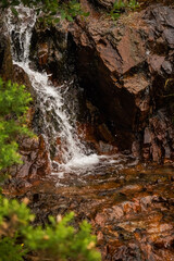 Small creek with water fall flows through very orange stones. Nature background.