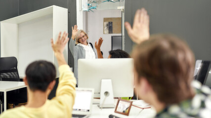 Cheerful aged woman, senior intern waving, saying goodbye to her young colleagues while leaving office after first day at work - obrazy, fototapety, plakaty