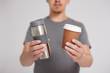 zero waste and eco friendly concept - young man comparing thermo cup with disposable paper coffee...