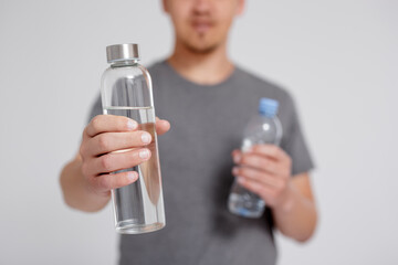 zero waste and eco friendly concept - man comparing water in reusable glass and plastic bottle over...