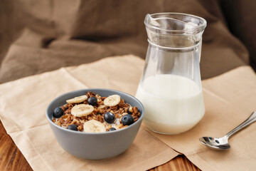 Close up of homemade granola in a plate with nuts, honey, blueberries and banana served on napkin, Fresh milk in glass jug