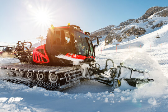 Red modern snowcat ratrack with snowplow snow grooming machine preparing ski slope piste hill at alpine skiing winter resort Ischgl in Austria. Heavy machinery mountain equipment track vehicle