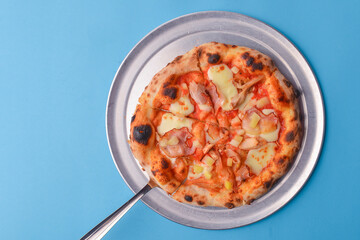 Whole Italian pizza with cheese and mushrooms on a metal tray over bright blue pastel bakcground.