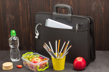 Black briefcase with phone and headphones. Bottle of water, notebooks with pens, lunch box of fruits, berries and nuts