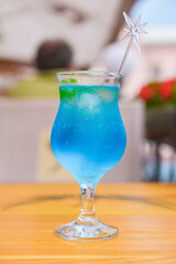 Blue curacao cocktail in a tall glass with a plastic straw outside. Delicious dessert drink, refreshing summer beverage.