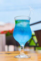 Blue curacao cocktail in a tall glass with a plastic straw outside. Delicious dessert drink, refreshing summer beverage.