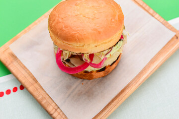 Home made burger on wooden tray over white table cloth and bright green background. Junk food, fast food concept.