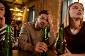 Close up of friends looking disappointed while watching sports match on TV together, drinking beer and cheering for team in the bar. People, leisure, friendship and entertainment concept