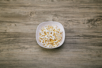 Popcorn in a white bowl top view. Fresh pop corn in white blow on wood table background. White Salty popcorn a full bowl.