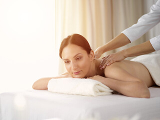 Fototapeta na wymiar Pretty brunette woman enjoying procedure of back massage in sunny spa salon. Beauty concept