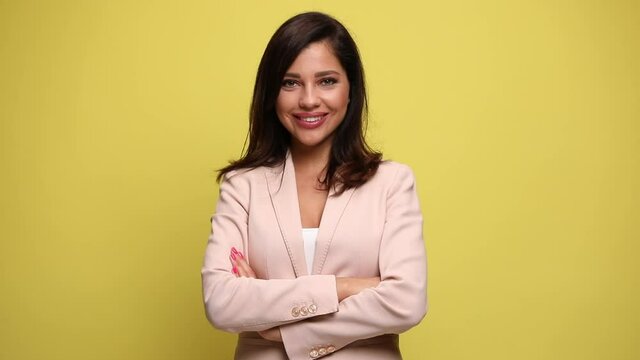 young businesswoman with a large smile on her face is crossing her arms and looking at the camera on yellow background