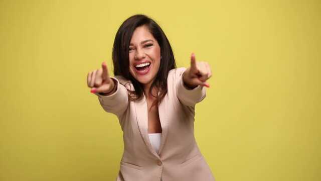 sexy young businesswoman full of excitement is raising her arms and dancing, pointing at the camera and celebrating succes on yellow background