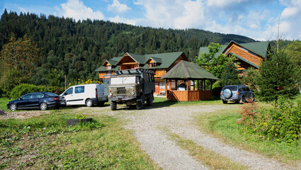 Many cars near the wooden cotage. Ecotourism in the mountains