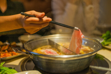 Hand using chopsticks pick raw sliced beef, vegetable, a piece of corn over the Chinese spicy hot pot, Szechuan Spicy Hot Pot