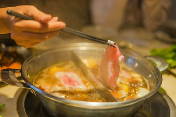 Hand using chopsticks pick raw sliced beef, vegetable, a piece of corn over the Chinese spicy hot pot, Szechuan Spicy Hot Pot